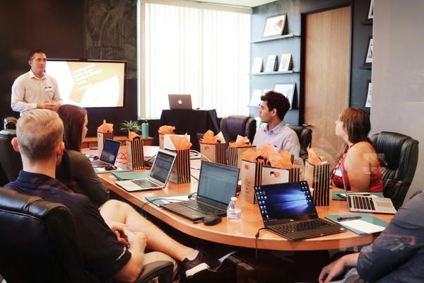 A team watching a presentation around a boardroom table with laptops