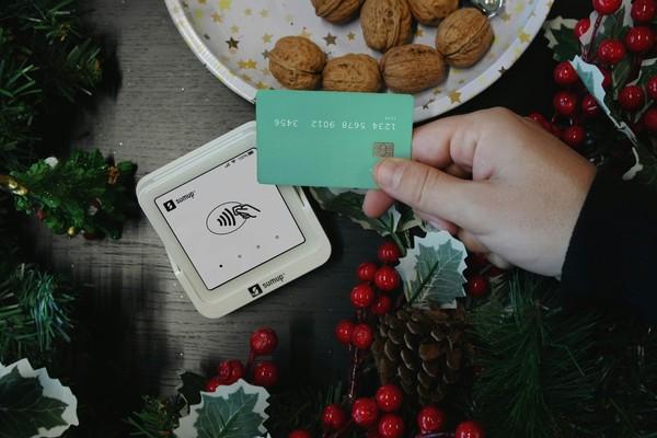 Hands holding a green bank card over a card reader beside festive decorations
