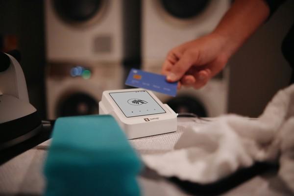 A hand tapping a bank card on a contactless payment terminal