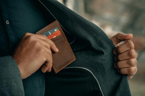 A person sliding a leather wallet into a coat pocket