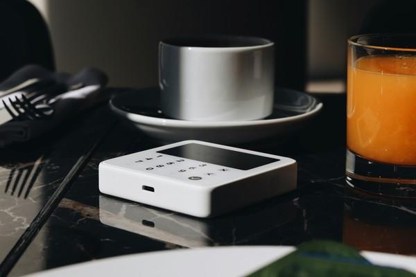 A coffee cup, juice glass and card reader on a dark table