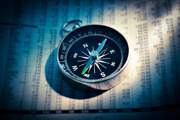 A compass resting on a printed page of financial figures